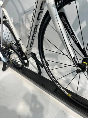 Detail eines weißen Simplon Rennrads auf einem schwarzen Ständer. Detail eines weißen Simplon Rennrads auf einem schwarzen Ständer.