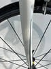 Detail einer weißen Fahrradgabel mit schwarzen Speichen.