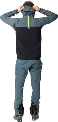 Mann mit Kapuze auf dem Rücken, in Skihose und -stiefeln.