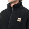 Ein Mann in einem schwarzen Fleece-Mantel mit Reißverschluss und Logo auf der Brust.