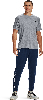 Ein Mann im grauen T-Shirt und dunkelblauer Jogginghose mit Logo steht vor weißem Hintergrund.