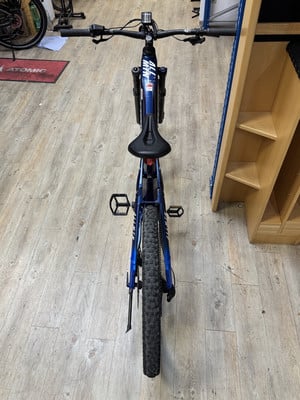Ein blaues E-Mountainbike mit schwarzem Sattel steht auf Holzboden. Ein blaues E-Mountainbike mit schwarzem Sattel steht auf Holzboden.