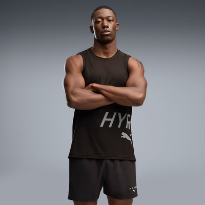 Ein Mann in einem schwarzen Tanktop und Shorts mit Puma-Logo steht mit verschränkten Armen da. Ein Mann in einem schwarzen Tanktop und Shorts mit Puma-Logo steht mit verschränkten Armen da.