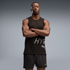 Ein Mann in einem schwarzen Tanktop und Shorts mit Puma-Logo steht mit verschränkten Armen da.