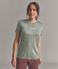 Eine Frau in einem grünen T-Shirt mit Bergen und einer roten Hose posiert vor grauem Hintergrund.
