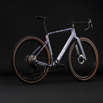 Lila Gravelbike mit buntem Rahmenaufdruck und braunen Reifen.