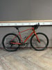 Ein orangefarbenes Gravelbike steht auf einem Holzboden vor einer grauen Wand.
