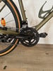 Detailaufnahme von Kurbel und Schaltwerk an einem grünen Fahrrad mit beigen Reifen.