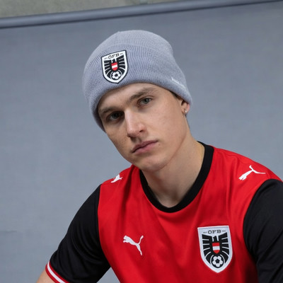 Junger Mann in grauem Hut mit Logo und rotem Fußballtrikot