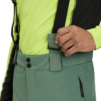Ein Mann schließt einen Klettverschluss an einem Hosenträger seiner Skihose.