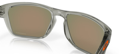 Transparente Brille mit verspiegelten Gläsern und orangefarbenem Oakley-Logo. Transparente Brille mit verspiegelten Gläsern und orangefarbenem Oakley-Logo.