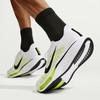 Férfi Nike futócipők fehér és neon színben, szürke háttérrel.