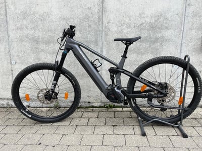 Graues Mountainbike mit Federung auf einem Ständer vor einer Wand.