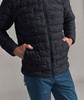 Ein Mann in einer dunklen Daunenjacke und blauen Hosen hat die Hände in den Taschen.