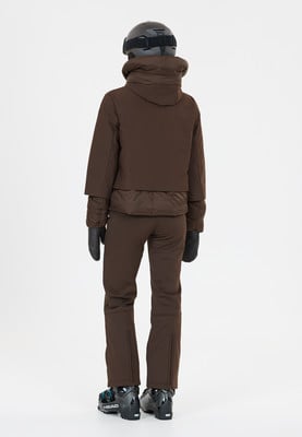 Eine Frau in brauner Skijacke, Hose, Helm und Handschuhen steht rückwärts. Eine Frau in brauner Skijacke, Hose, Helm und Handschuhen steht rückwärts.