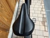 Schwarzer Fahrradsattel mit perforierter Oberfläche auf Pflastersteinen.