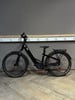 Ein schwarzes Winora E-Bike steht auf einem Holzboden vor einer grauen Wand.