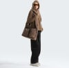 Model in brauner Kapuzenjacke und schwarzer Hose mit Umhängetasche.