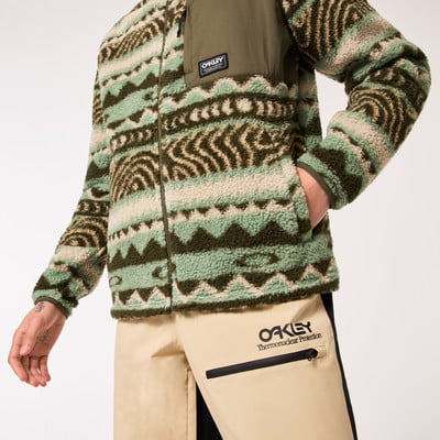 Ein Mann in einem warmen Fleece-Pullover mit Ethno-Muster und einer beigen Hose mit Logo.