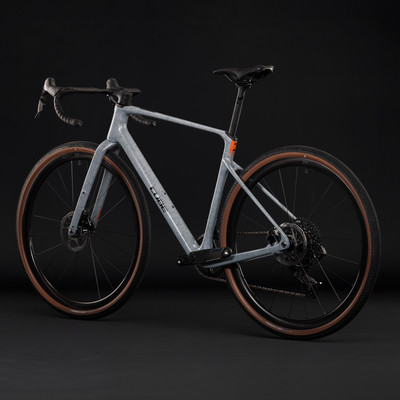 Graues Gravelbike mit braunen Reifen und schwarzen Felgen vor dunklem Hintergrund. Graues Gravelbike mit braunen Reifen und schwarzen Felgen vor dunklem Hintergrund.