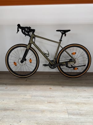 Ein grünes Fahrrad mit schwarzen Details steht auf einem Holzboden vor einer weißen Wand. Ein grünes Fahrrad mit schwarzen Details steht auf einem Holzboden vor einer weißen Wand.
