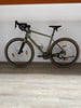 Ein grünes Fahrrad mit schwarzen Details steht auf einem Holzboden vor einer weißen Wand.