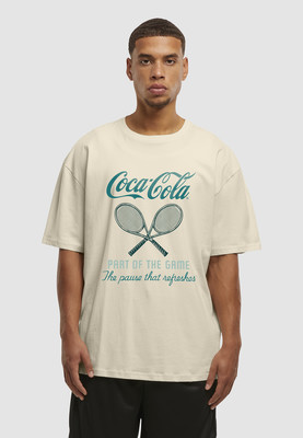 Ein Mann in einem beigefarbenen T-Shirt mit Coca-Cola-Logo und Tennisschlägern.
