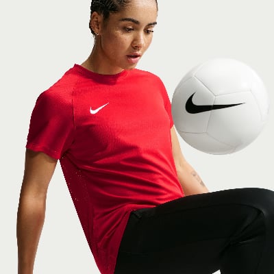Eine Frau in einem roten Hemd mit einem Nike-Ball vor einem hellgrauen Hintergrund.
