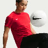 Eine Frau in einem roten Hemd mit einem Nike-Ball vor einem hellgrauen Hintergrund.