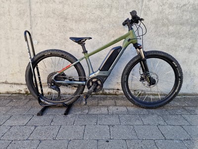 Ein grünes E-Bike steht vor einer Betonwand auf Pflastersteinen. Ein grünes E-Bike steht vor einer Betonwand auf Pflastersteinen.
