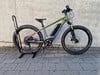 Ein grünes E-Bike steht vor einer Betonwand auf Pflastersteinen.