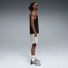 Ein Mann in schwarzem Tanktop und hellen Shorts mit Turnschuhen vor grauem Hintergrund.