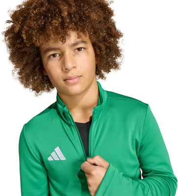 Ein Junge mit lockigem Haar trägt einen grünen Hoodie mit Adidas-Logo.
