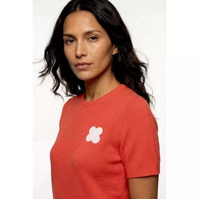 Eine Frau in einem orangefarbenen Pullover mit einer weißen Blume auf der Brust. Eine Frau in einem orangefarbenen Pullover mit einer weißen Blume auf der Brust.