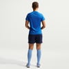 Rückansicht einer Frau in blauem T-Shirt, dunkler Hose und hellblauen Socken.