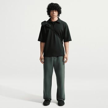 Mann in schwarzem Poloshirt und grüner Hose mit Umhängetasche.