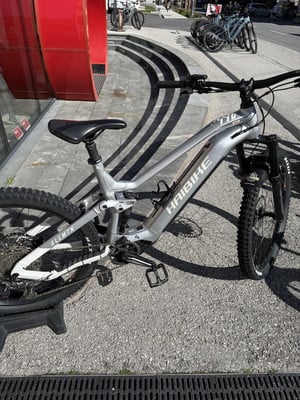 Graues Haibike E-Mountainbike, geparkt neben einem roten Gebäude. Graues Haibike E-Mountainbike, geparkt neben einem roten Gebäude.