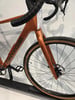 Ein orangefarbenes Gravelbike mit grauen Lenkern und schwarzen Reifen.