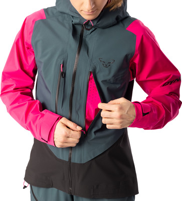 Eine Frau öffnet eine pinke Jacke mit grauen und schwarzen Einsätzen.