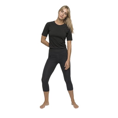 Eine Frau in einem dunklen T-Shirt und 3/4-Hose steht auf weißem Grund.