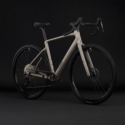 Ein beiges Cube Gravelbike mit schwarzen Rädern und Details vor dunklem Hintergrund. Ein beiges Cube Gravelbike mit schwarzen Rädern und Details vor dunklem Hintergrund.