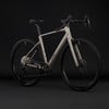 Ein beiges Cube Gravelbike mit schwarzen Rädern und Details vor dunklem Hintergrund.