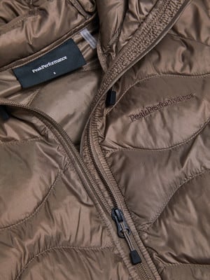 Detail einer braunen Peak Performance Jacke mit Logo und Reißverschluss.