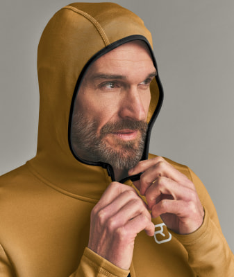 Ein Mann schließt eine gelbe Kapuzenjacke mit schwarzer Paspel. Ein Mann schließt eine gelbe Kapuzenjacke mit schwarzer Paspel.