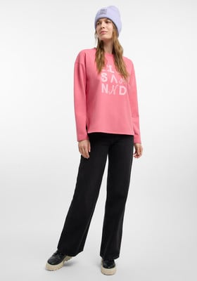 Junge Frau in pinkem Pullover und schwarzer Jeans mit lila Mütze. Junge Frau in pinkem Pullover und schwarzer Jeans mit lila Mütze.
