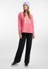 Junge Frau in pinkem Pullover und schwarzer Jeans mit lila Mütze.