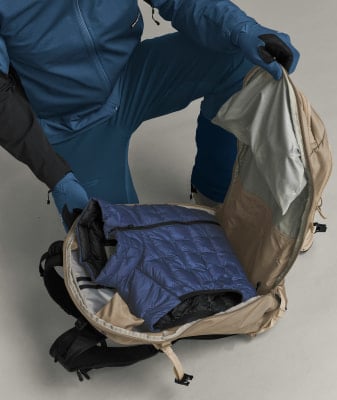 Eine Person packt eine blaue Daunenjacke in einen Rucksack. Eine Person packt eine blaue Daunenjacke in einen Rucksack.