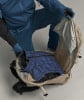 Eine Person packt eine blaue Daunenjacke in einen Rucksack.