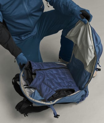 Eine Person in blauer Kleidung packt eine blaue Daunenweste in einen Rucksack. Eine Person in blauer Kleidung packt eine blaue Daunenweste in einen Rucksack.
