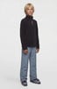 Junge in schwarzem Fleece-Pullover und blauer Skihose.